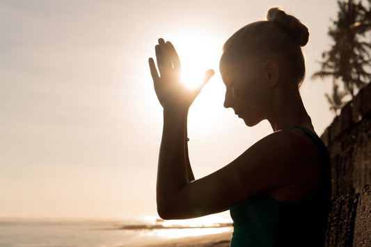 Woman meditating by the ocean at sunrise practicing mindfulness to build inner resilience, reduce stress, and support emotional balance