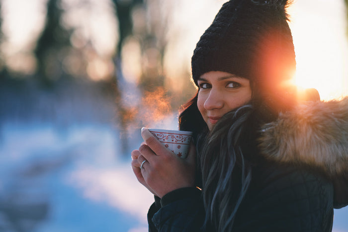 Woman enjoying a warm herbal drink outdoors on a chilly fall morning, supporting joint comfort and seasonal warmth