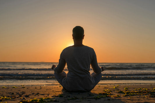 Person meditating on a quiet beach at sunrise, illustrating the gradual journey toward calm, resilience, and overall well-being.