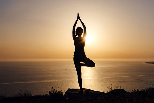 Silhouette of person practicing yoga at sunrise by the sea, symbolizing mindfulness, balance, and inner vitality.