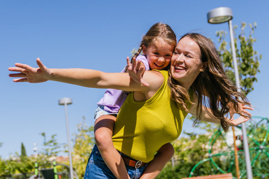 Mother carrying smiling child outdoors, representing family wellness, energy, and maintaining an active healthy lifestyle together.