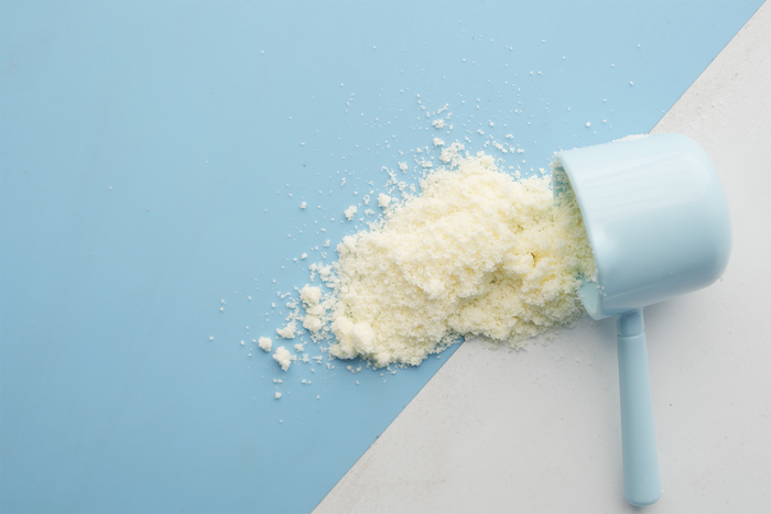 Close-up of colostrum powder spilled from a scoop on a blue background, representing supplement preparation and daily wellness use.