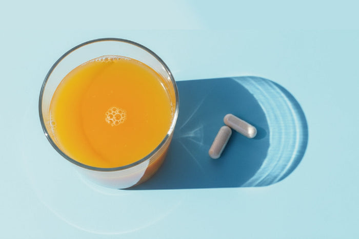 Glass of orange juice with zinc supplement capsules on a light blue background, representing daily zinc intake and nutritional support.