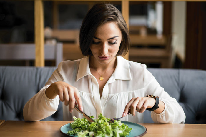 Woman practicing mindful eating, slowly enjoying a fresh green salad at a table, promoting healthy digestion and balanced nutrition.