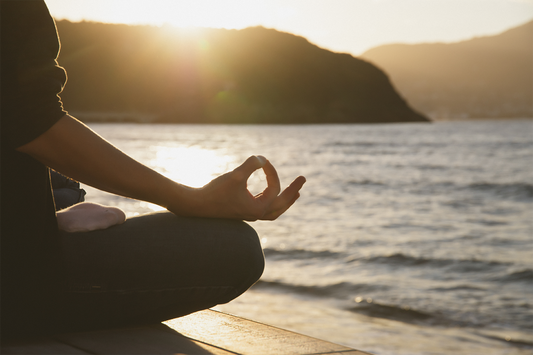 Person meditating peacefully by the ocean symbolizing mindfulness inner balance and Ayurvedic mind-body wellness practices