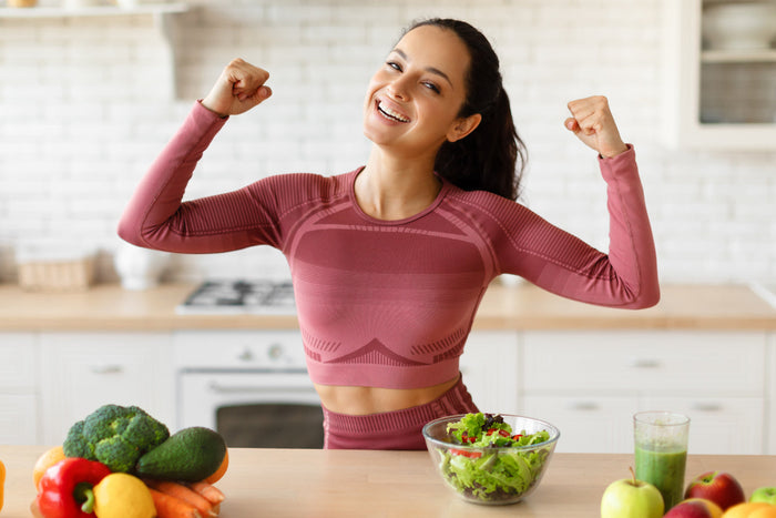 Smiling woman celebrating a healthy lifestyle with fresh vegetables, salad, and daily wellness habits that support energy and overall vitality.