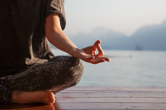 Person meditating by the water at sunrise, symbolizing Ojas in Ayurveda and the connection between inner vitality, balance and wellness.