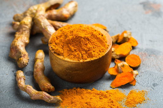 Bright yellow curcumin powder in a bowl surrounded by turmeric roots, illustrating the active compound found in turmeric.