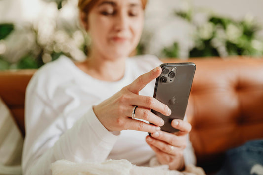 Woman relaxing on a sofa while scrolling her phone, representing mindful screen use during a digital detox
