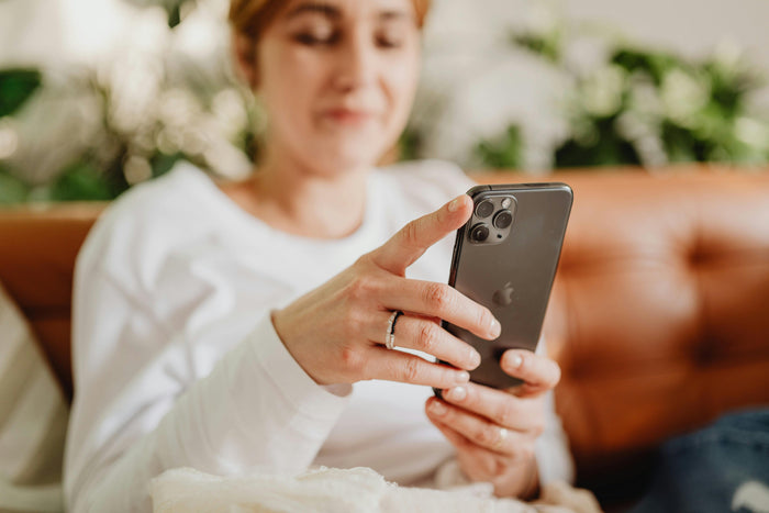Woman relaxing on a sofa while scrolling her phone, representing mindful screen use during a digital detox