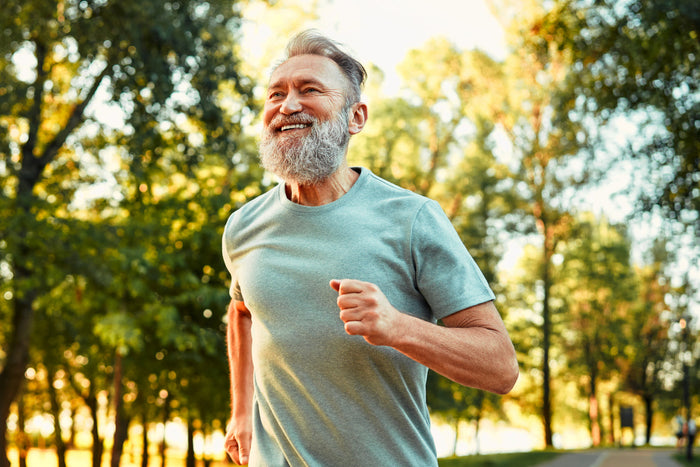 Active older man jogging outdoors in a sunny park, illustrating daily movement and healthy lifestyle habits that support cellular wellness