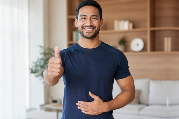 Smiling man giving a thumbs-up while holding his stomach, representing digestive comfort, immune wellness, and overall health supported by colostrum.